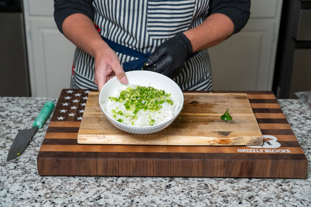 a person tilting up a white bowl filled with diced raw white onion and jalapeno