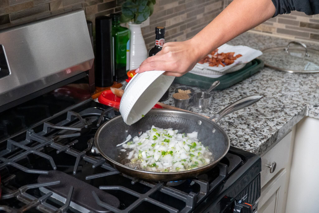 a person tipping raw white onion and jalapeno into a fry pan