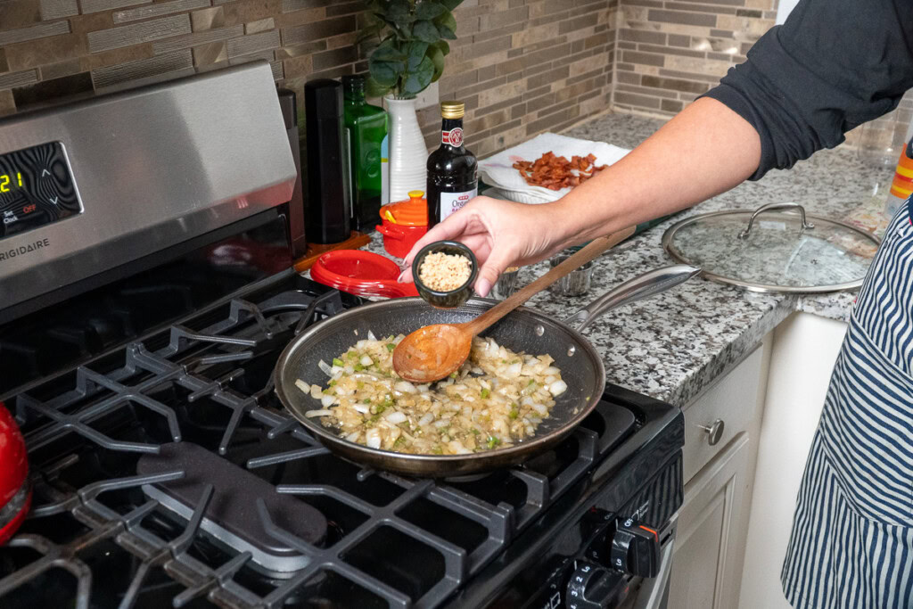 a hand tipping a small container of garlic into a fry pan