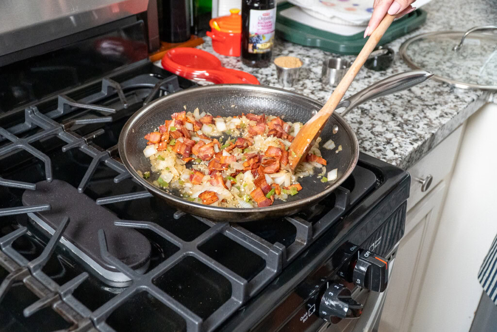 bacon back in the frying pan with the onions being stirred with a wooden spoon
