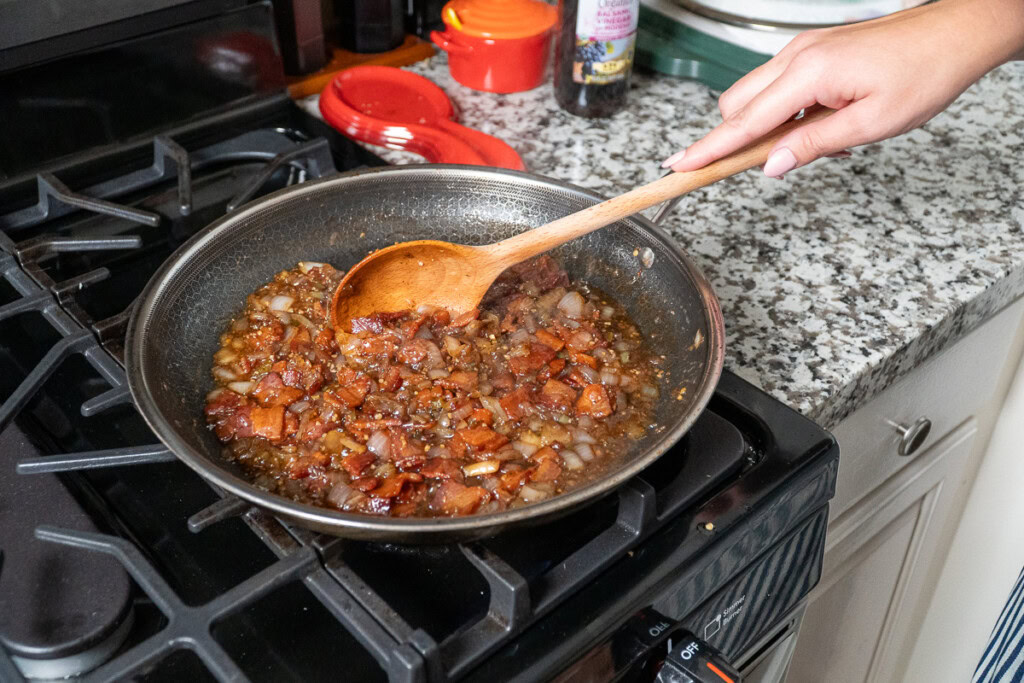 bacon jam cooking in a frypan with a wooden spoon stirring it