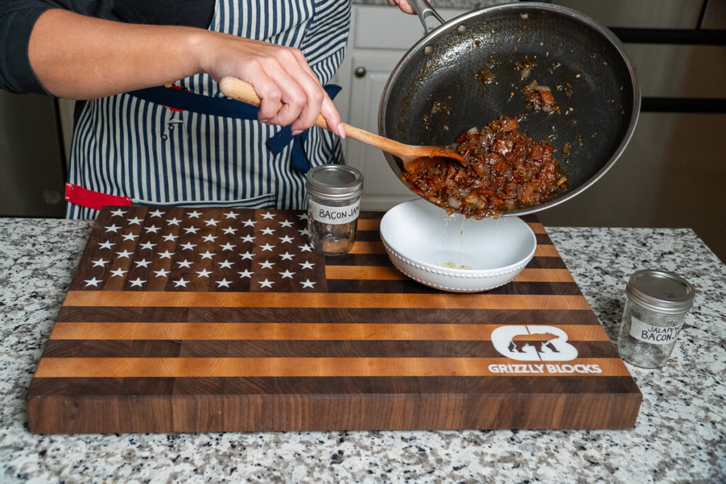 bacon jam being poured from the frypan to a white bowl by a wooden spoon