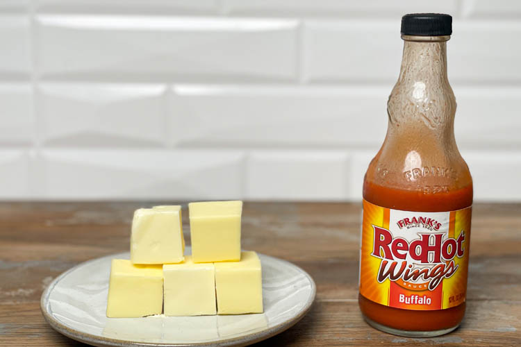 white plate with butter cubes and a bottle of franks hot sauce on wooden board