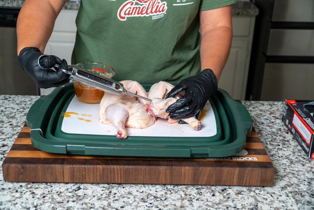 a person injecting a raw chicken with juicy goodness