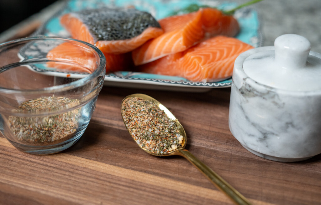 spoonful of salmon rub on table with jar of rub and filets of raw salmon in the background