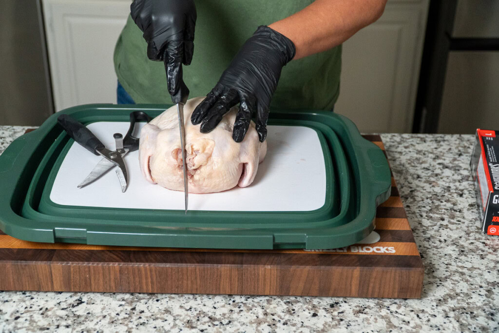 a person slicing down the side of the backbone on a raw chicken