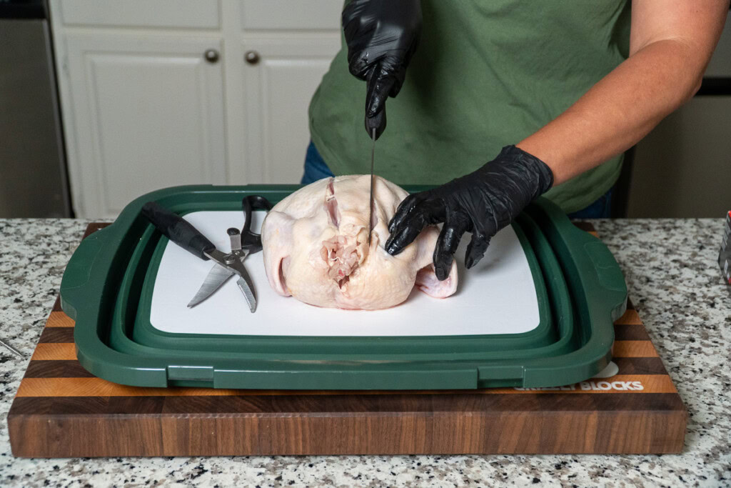 a person slicing a line down the side of the backbone of a raw chicken