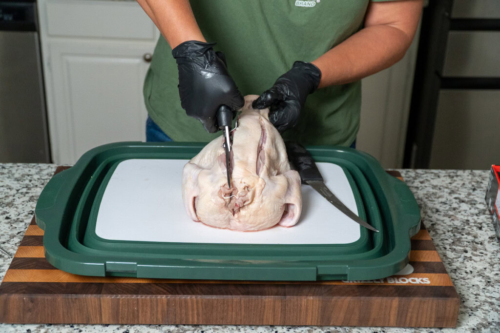 a person with shears cutting the backboneout of a raw chicken