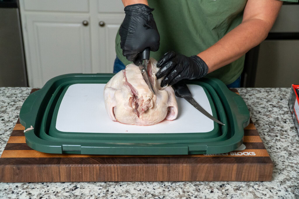a person with shears is cutting the backbone out of a raw chicken