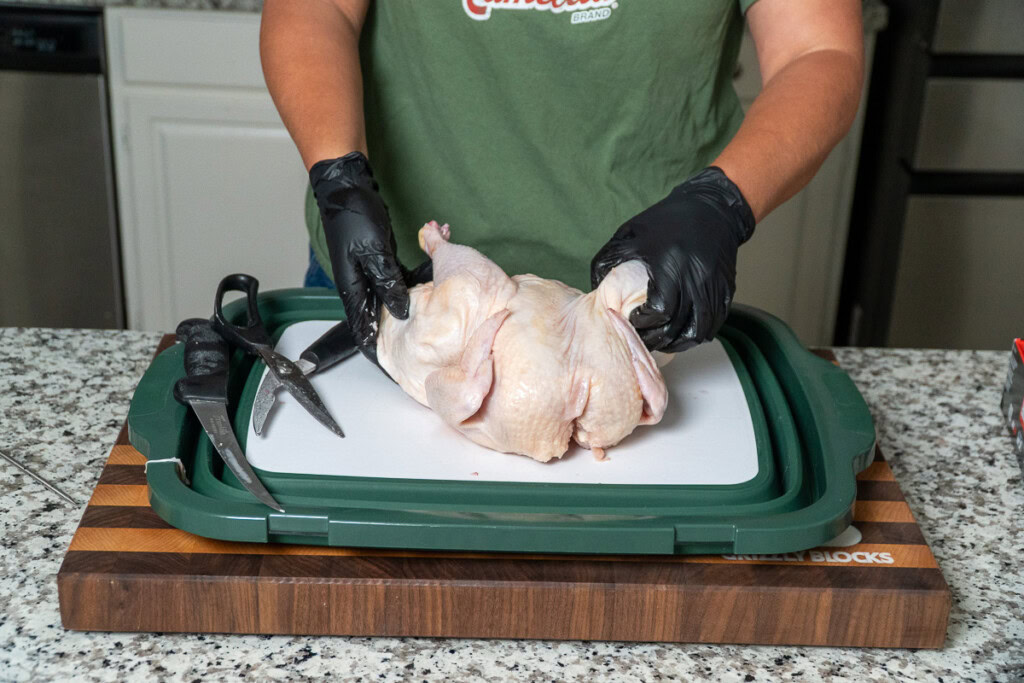 a person attempting to spread out a spatchcocked raw chicken