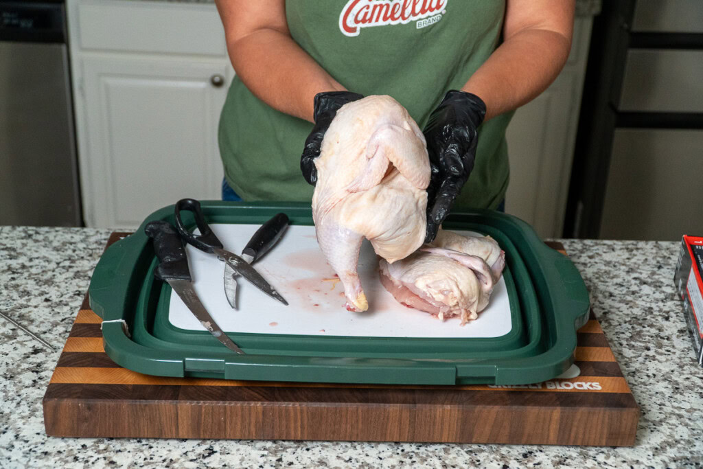 a person holding up a half a raw chicken she just cut up