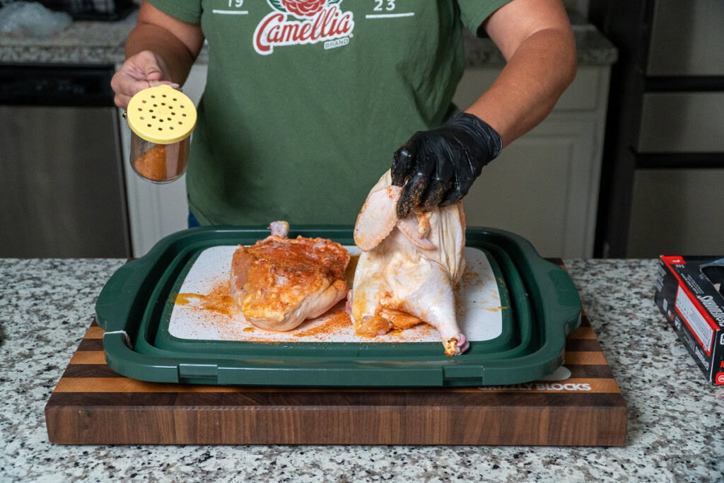 a person flipping a raw chicken half off a board for seasoning