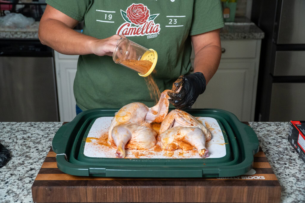 a person sprinkling seasoning all over a raw chicken