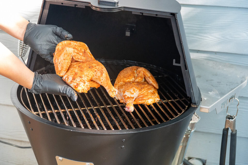 a person putting raw seasoned chicken halves on the grilla grill pellet smoker