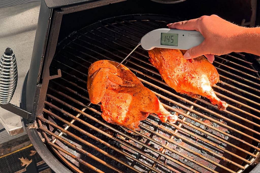 a temperature probe stuck in a chicken on the grill reading 145