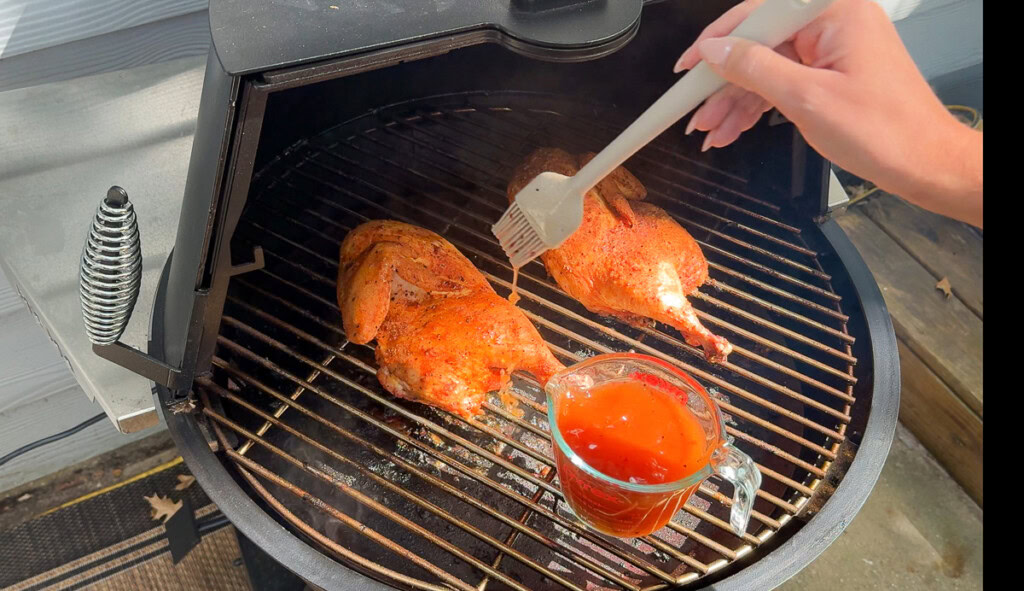 chicken on the smoker being brushed with bbq sauce