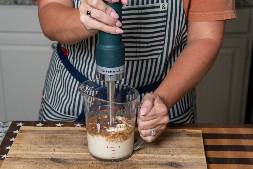 a person with an imersion blender, blending salad dressing ingredients