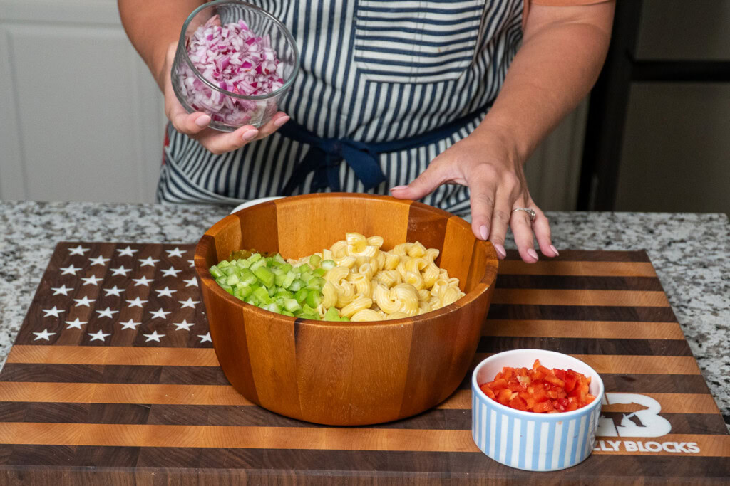 a wooden bowl of cooked pasta with a bowl of diced red onion being tipped in