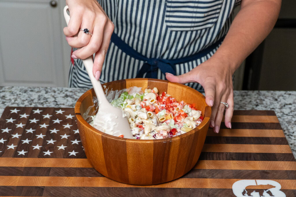 a person stirring salad dressing through macaroni salad