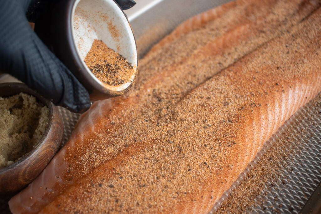a bowl of bbq rub being sprinkled over a raw salmon filet