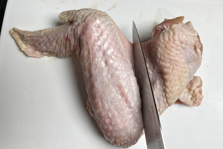 knife cutting a raw chicken wing
