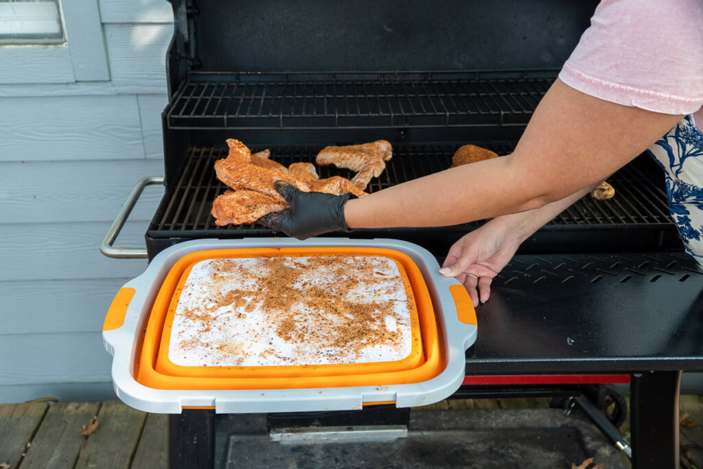 a person wearing a black glove placing raw seasoned turkey wings on the smoker