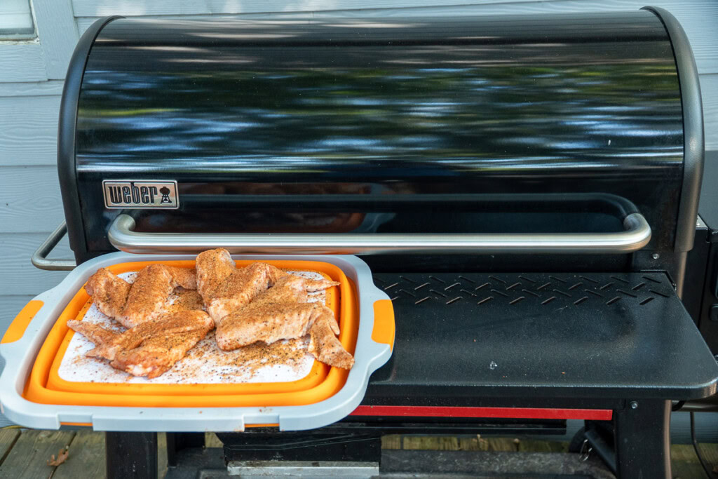 raw seasoned turkey wings on a white board sitting on  the smoker