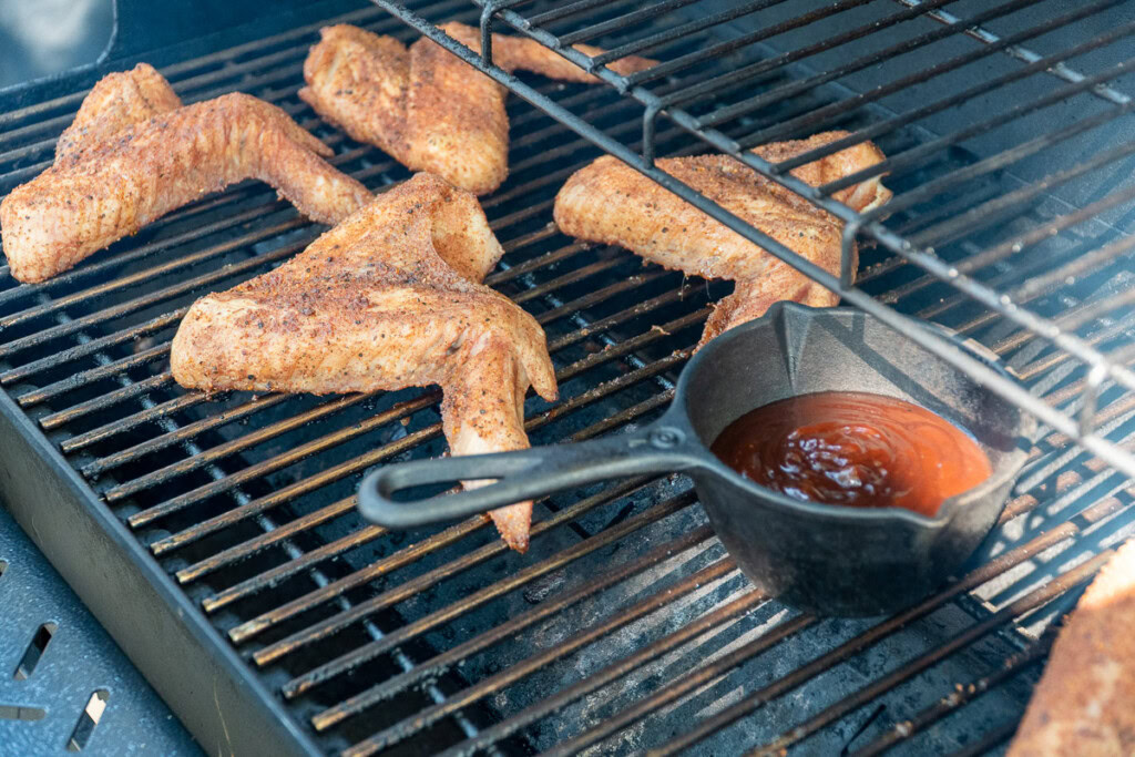 cooked turkey wings and a pot of sauce on the smoker