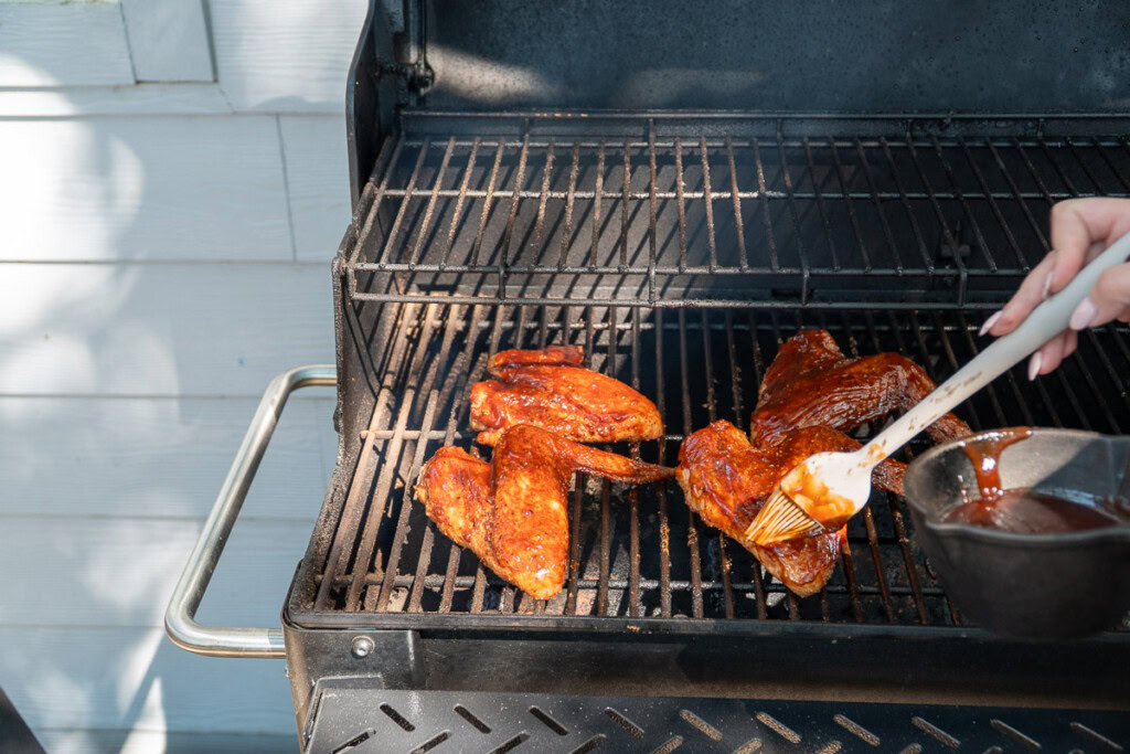 a person basting smoked turkey wings with sauce