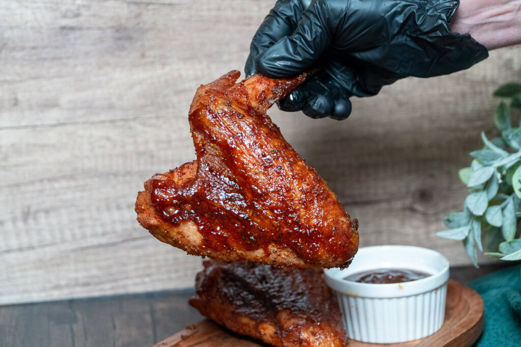 a black gloved hand holding a single sauced wing up