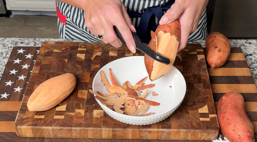 a person peeling raw sweet potatoes with a vegetable peeler