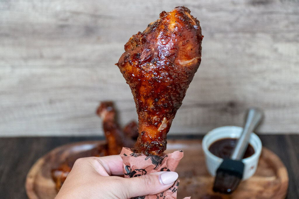 a hand holding up a saucy smoked turkey leg 