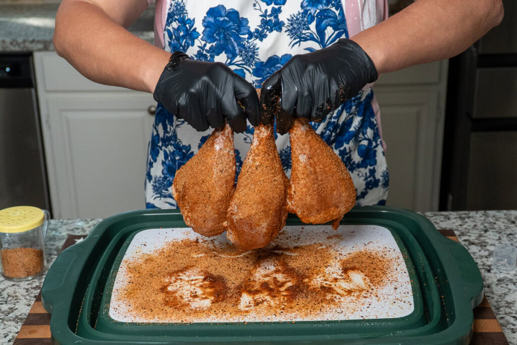 a person holding three raw seasoned turkey legs up in the air