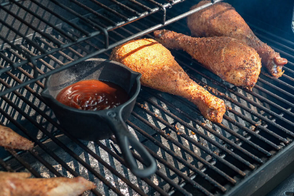 a small pot of bbq sauce and turkey legs on the smoker