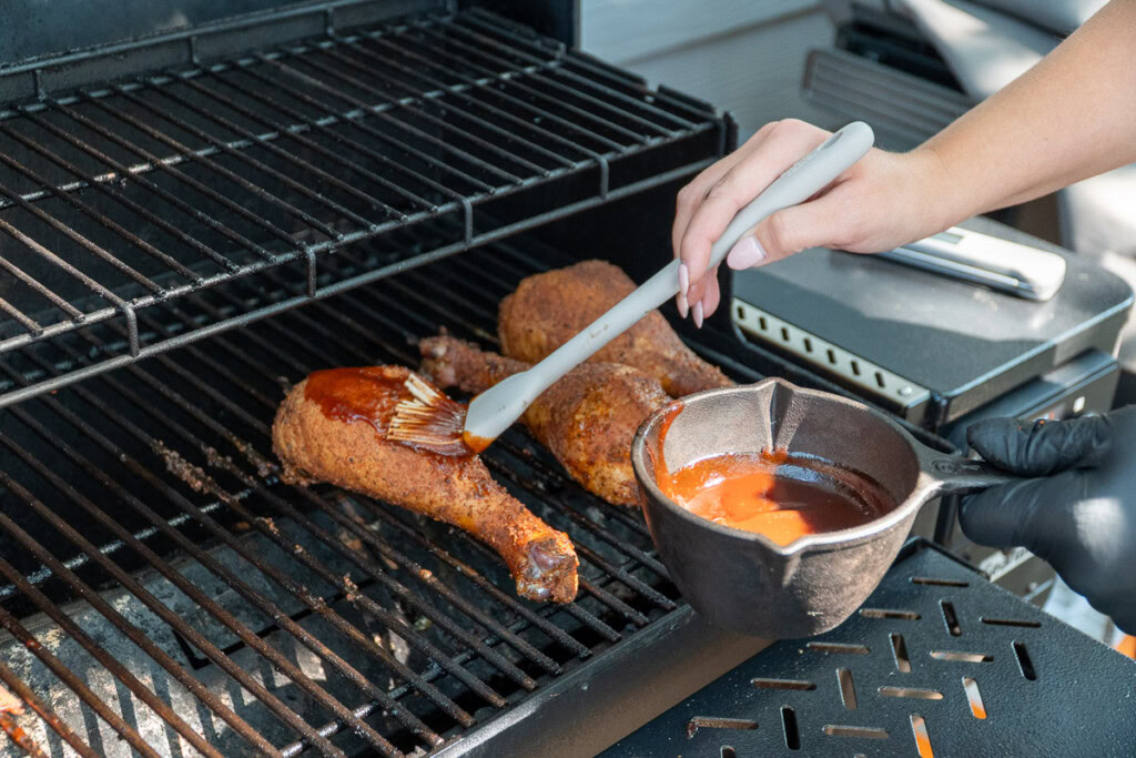 a person basting a turkey leg with BBQ sauce