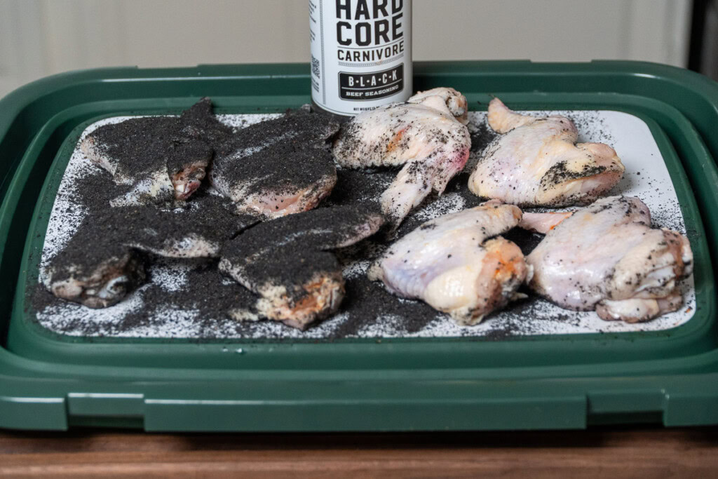 a tray of raw chicken wings with half of them coated with black BBQ rub