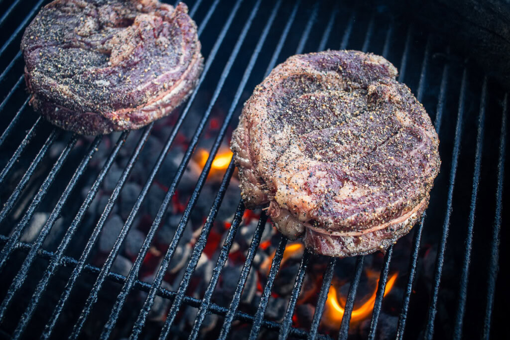 raw seasoned chuck eye steak on the grill with hot coals underneath