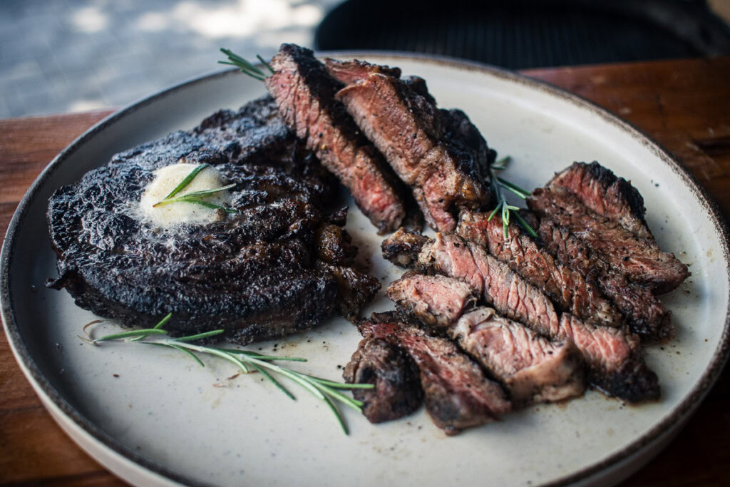 one whole piece of chuck eye steak and one sliced piece on a wooden board