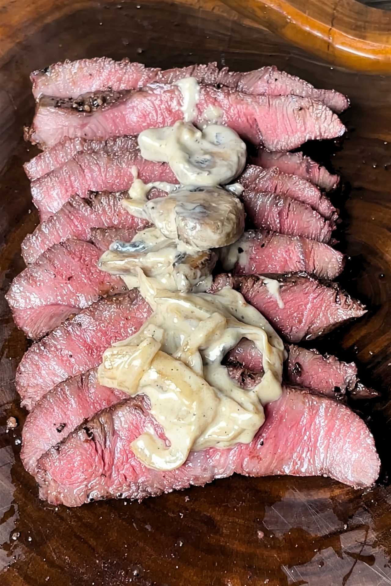 grilled flat iron steak sliced topped with mushroom sauce on a wooden board