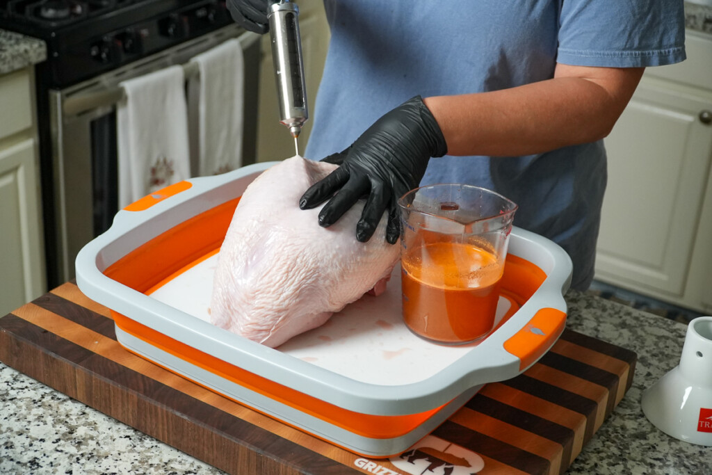 a black gloved hand holding the turkey while it is being injected with an injector