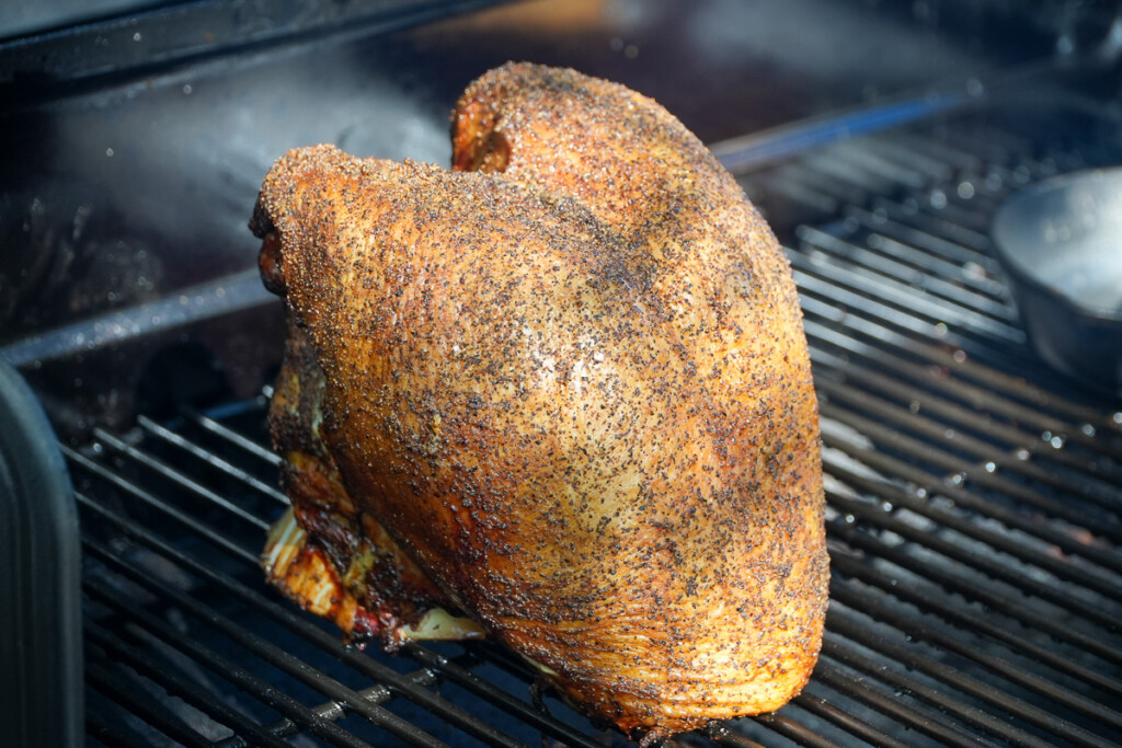 a seasoned turkey breast on a beer can holder in the smoker