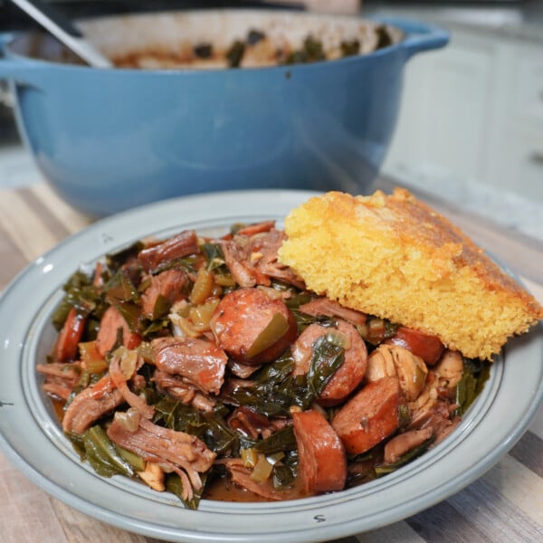 Collard Greens Cajun Gumbo plated with a cornbread wedge and blue pot in the background.