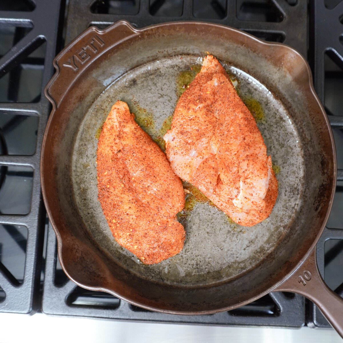 Seasoned chicken breast on skillet over stove top for the Creamy Chicken Enchilada Skillet recipe.