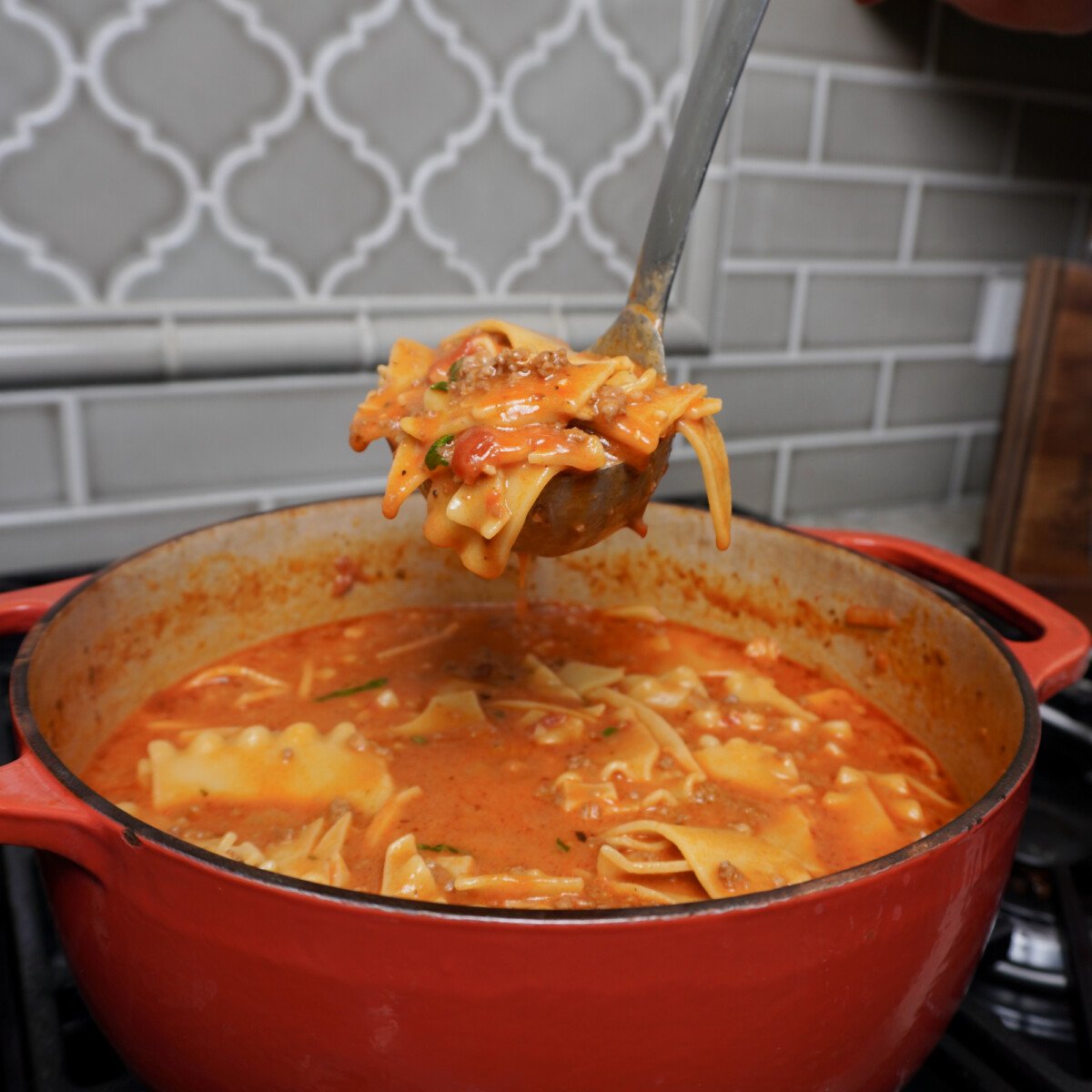 Ladle full of Lasagna soup over a dutch oven.