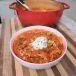 Lasagna soup plated in a white bowl on a stripped cutting board with ricotta cheese on top.