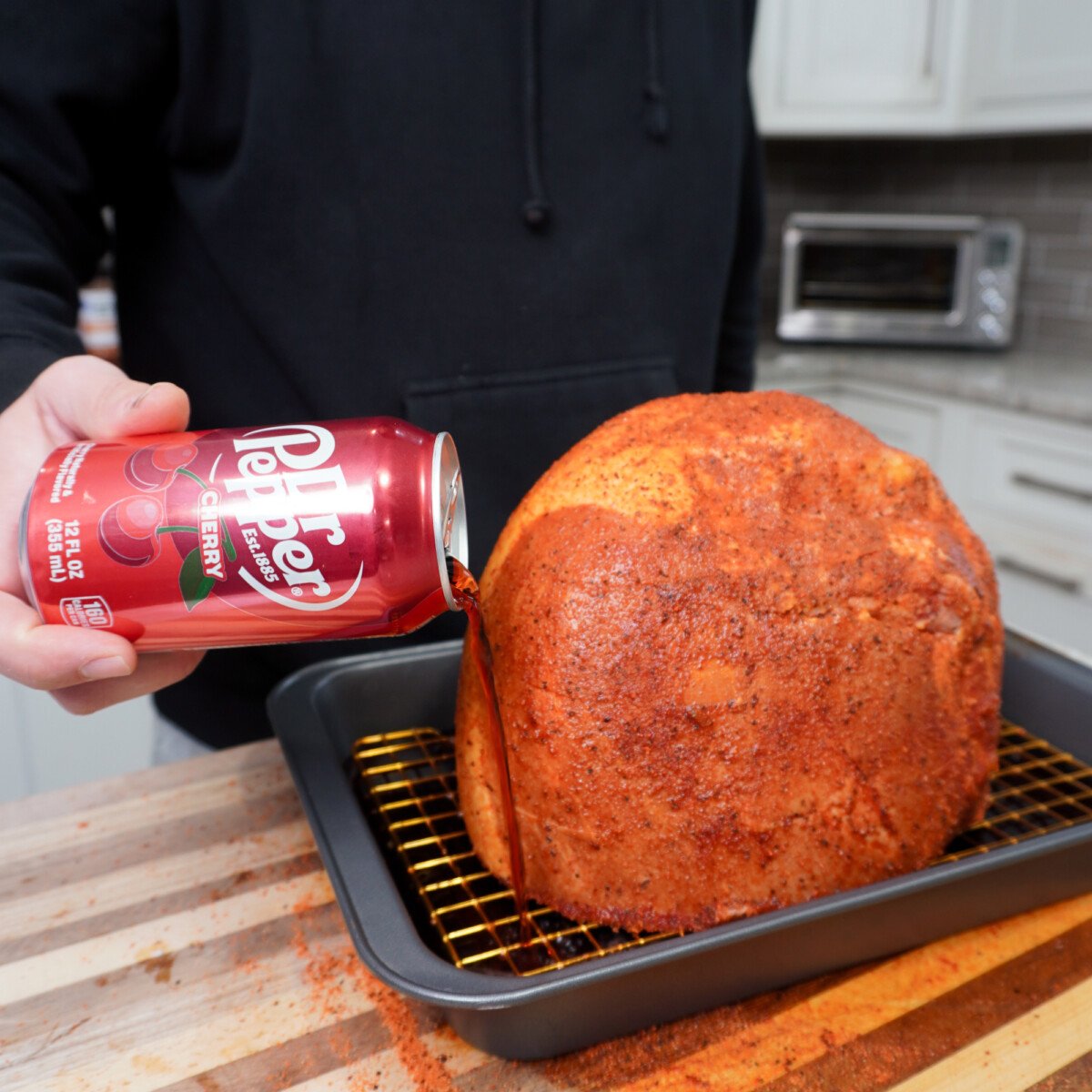 pouring cherry dr. pepper into the pan under the seasoned ham.