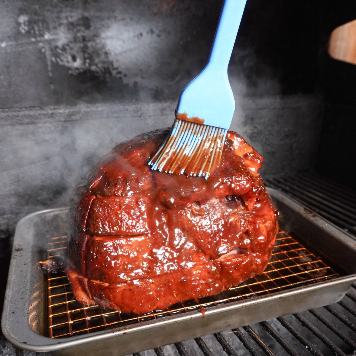 glazing the smoked ham with cherry dr. pepper sauce on the smoker.