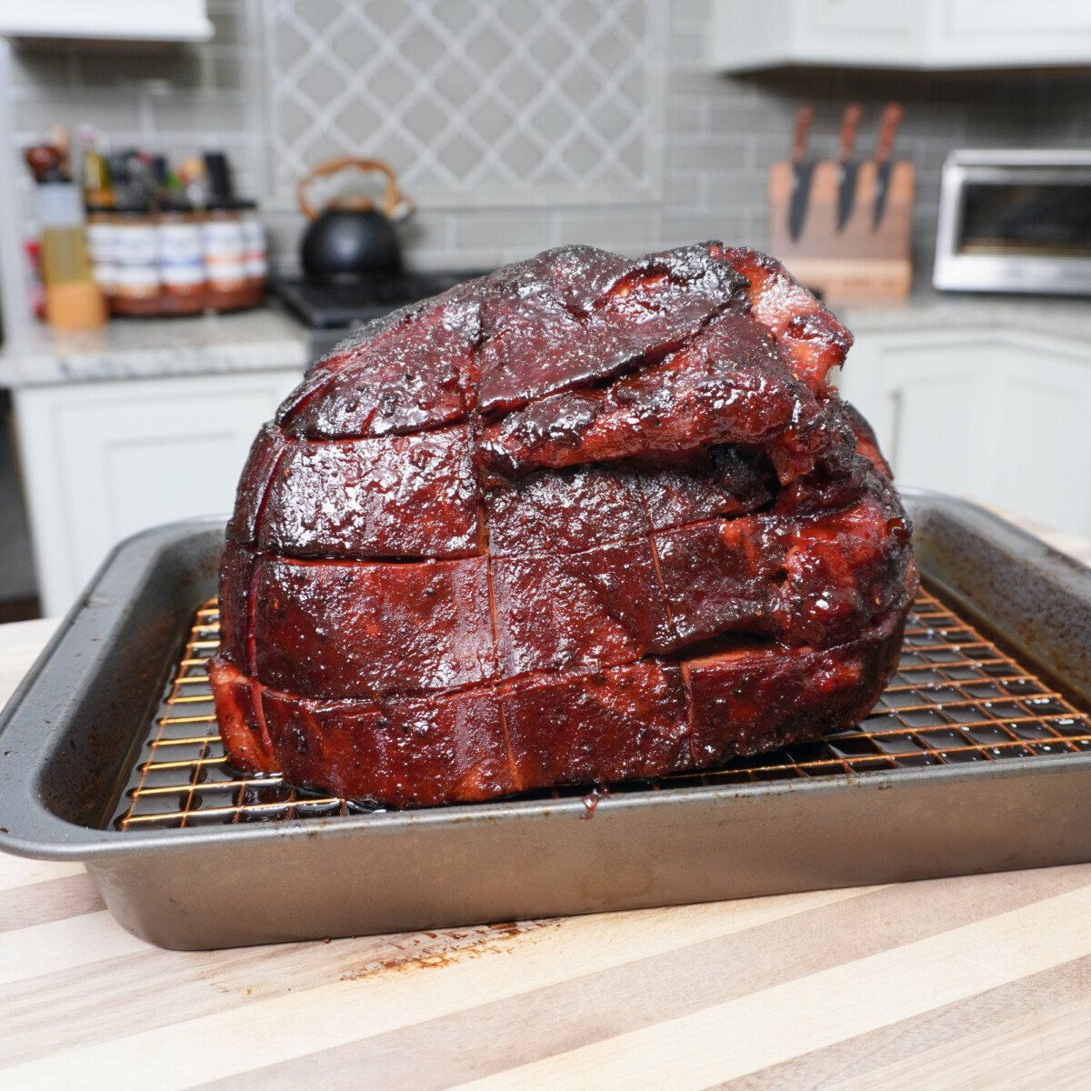 smoked ham with cherry dr. pepper sauce on wire rack with kitchen in the background.