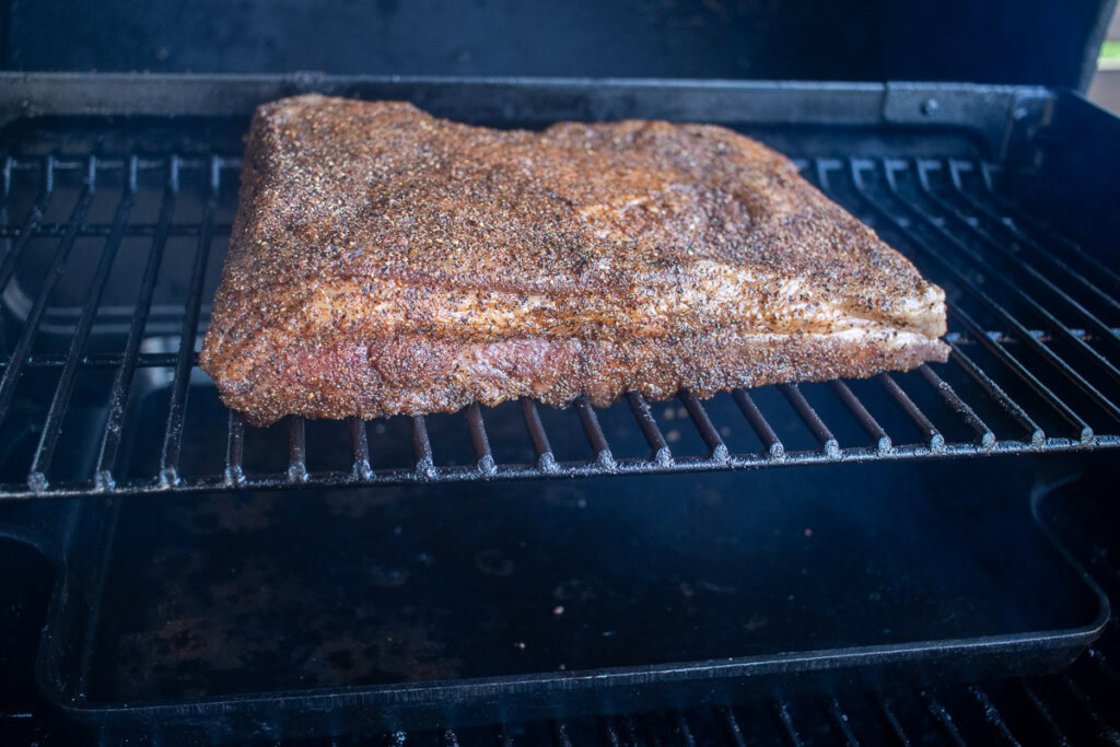 a raw seasoned piece of beef belly in the traeger ironwood