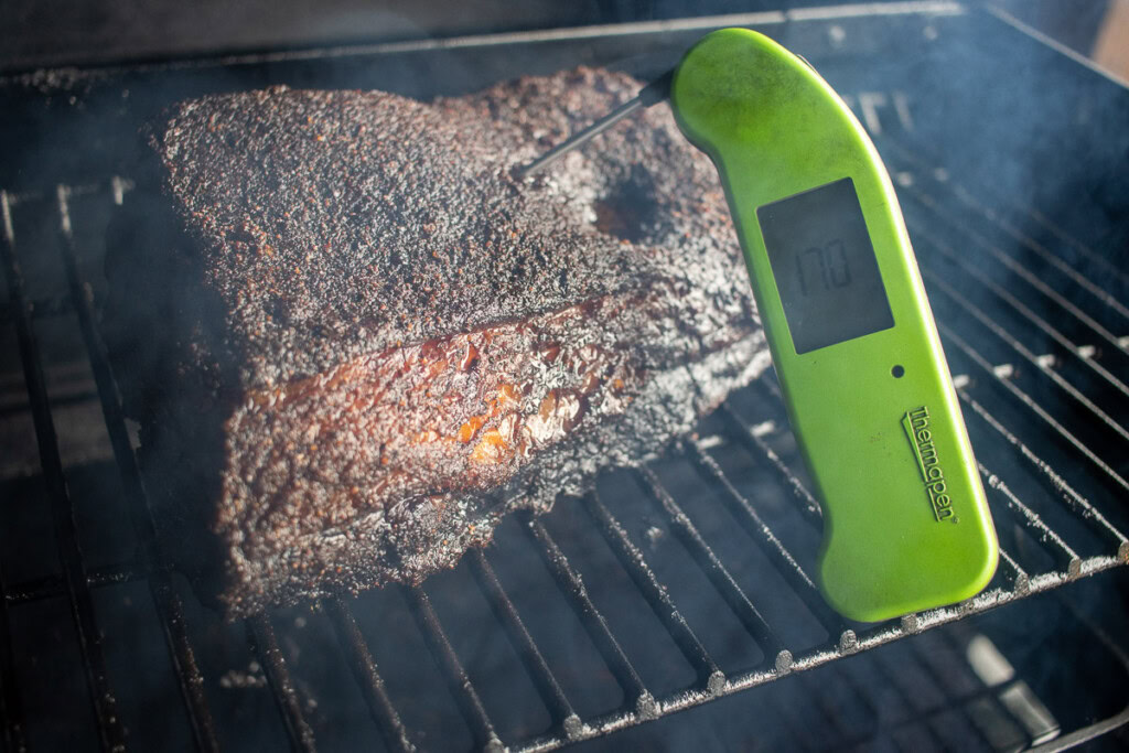 a piece of smoked beef belly with an instant read thermometer inserted reading 170F